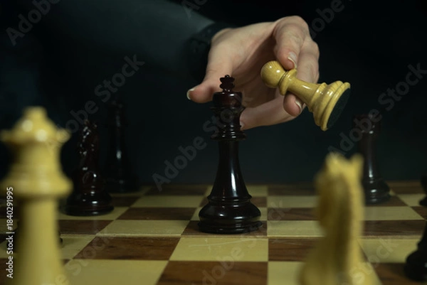 Obraz Chess player moves pawn to capture king during a game in a dimly lit room in the evening