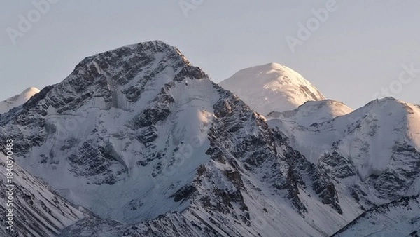 Fototapeta Stunning view of towering snow-covered mountains illuminated by soft morning light, showcasing rugged peaks and serene atmosphere, creating a breathtaking natural landscape experience