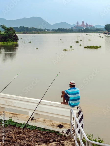 Obraz Elderly fisherman at side of river during sunset and catching fish with spinning. Senior fisherman with fishing rods on footbridge near the lake at summer. Mature man fishing on lake. Adult lifestyle.