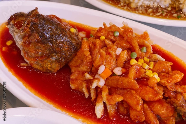 Fototapeta A close-up of a large deep-fried fish fillet (or fish head) generously covered in a bright red sweet and sour chili sauce.
