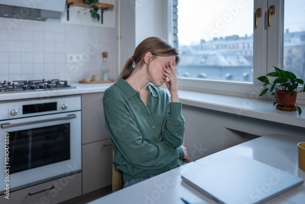 Fototapeta Exhausted woman covering face with hand feels burnout, drained, sits at table in front of closed laptop. Tired female with mental fatigue, emotional pressure, anxiety caused by workload, life problems