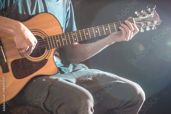 Fototapeta the hand of man playing acoustic guitar, close-up, flash of light, a beautiful light in the background