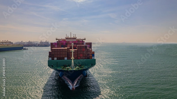 Fototapeta A container ship, fully loaded with goods, sails out to sea, delivering products to various locations around the world.
