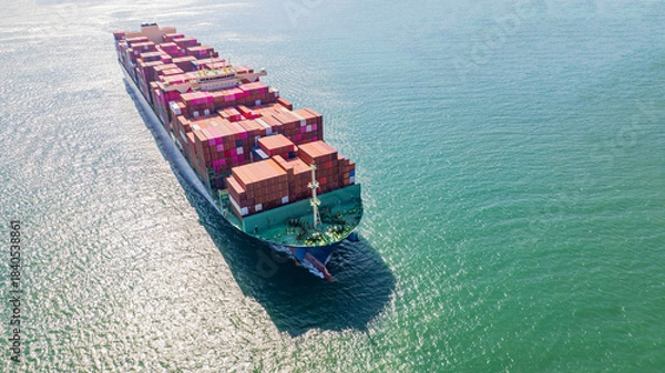 Fototapeta A container ship, fully loaded with goods, sails out to sea, delivering products to various locations around the world.