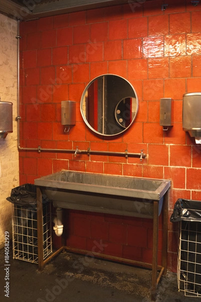 Fototapeta Industrial-Style Bathroom Features a Metal Sink, Circular Mirror, and Bright Red Tile Wall in a Modern Urban Setting