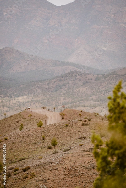 Obraz Vertical image of a mountain landscape with with sandy bare hills surrounded by desert greenery outdoor aon a foggy day in the Australian outback in Flinders Ranges in Australia with space for text.
