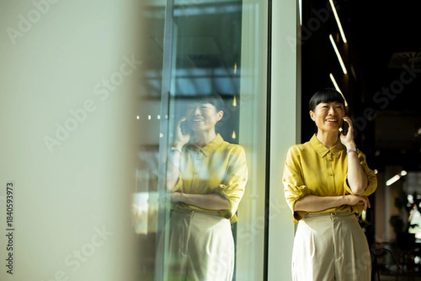 Fototapeta Woman in yellow shirt enjoys a phone conversation in a bright cafe