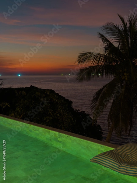 Fototapeta View from luxury villa at dusk, pool lighting, sun loungers for sunbathing, umbrellas from the sun, pillows for swimming in the pool, palm tree on background