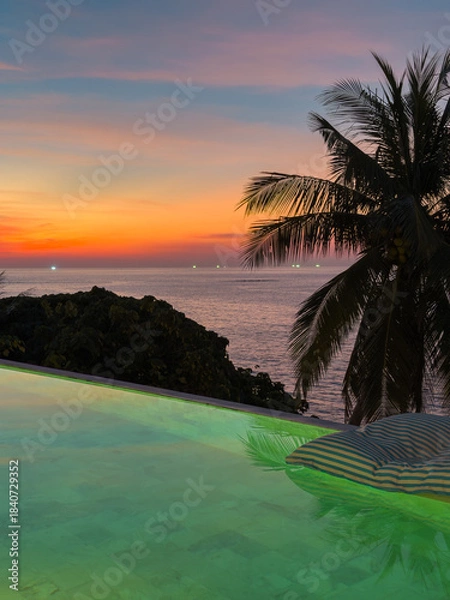 Fototapeta View from luxury villa at dusk, pool lighting, sun loungers for sunbathing, umbrellas from the sun, pillows for swimming in the pool, palm tree on background
