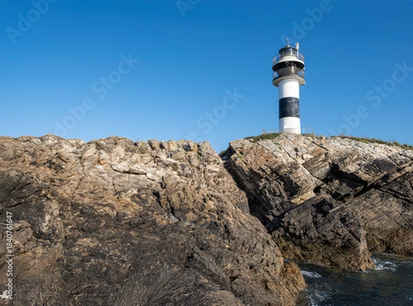 Obraz black and white lighthouse standing on a rocky cliff by the deep blue sea under a clear sky, Isla Pancha, Ribadeo, Galicia, Spain