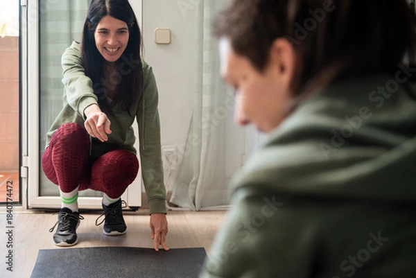 Fototapeta Two friends are working out together at home in a bright, relaxed environment. One of them smiles while guiding and encouraging the other, creating a natural scene that conveys support, motivation, an