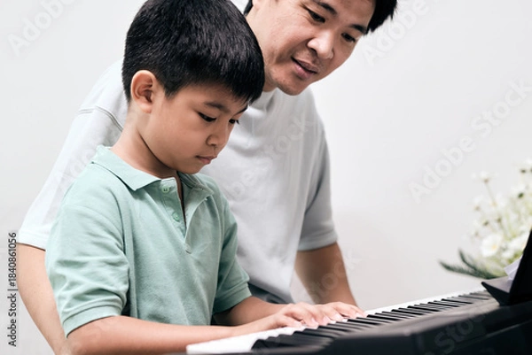 Obraz Child learning to play the keyboard with guidance from father, highlighting music education, skill development, and supportive family interaction in warm home
