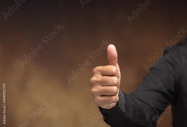 Obraz Hand showing thumbs up gesture on brown background.