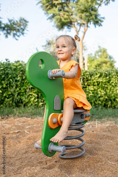 Fototapeta young girl plays on green spring rider in a playground