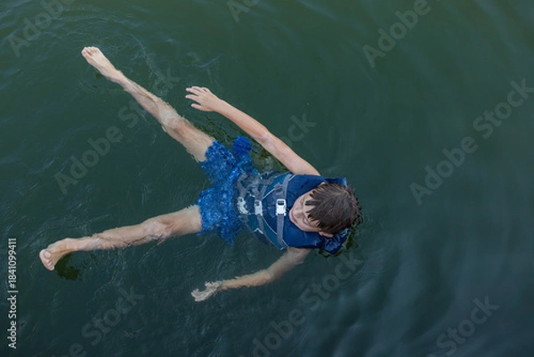 Obraz boy in lifejacket floating on calm lake