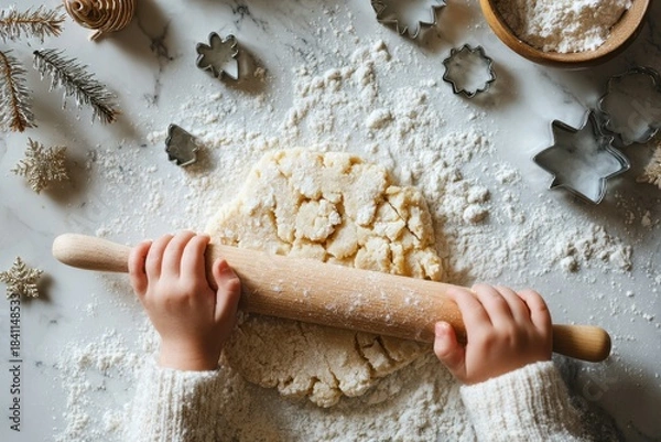 Fototapeta child rolling cookie dough on floured marble countertop with wooden rolling pin, metal cutters and evergreen sprig — Christmas cookie baking