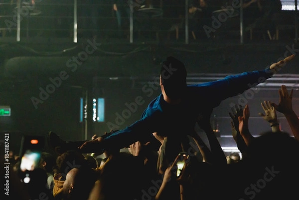 Fototapeta Young person lifted by audience during an energetic live music event with cheering crowd and dynamic lighting.