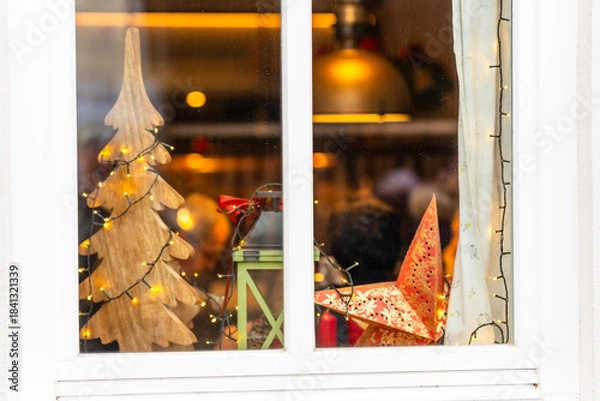 Fototapeta A beautifully decorated window glowing with Christmas motifs and twinkling evening lights creating a warm festive atmosphere outdoors