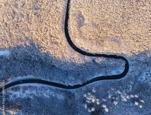 Fototapeta Aerial view of winter landscape with snow covered mountain hills and winding forest road in morning