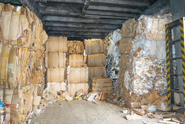 Obraz Large stacks of compressed paper blocks are piled high inside a dark industrial building. The paper appears to be waste material ready for recycling at the paper mill