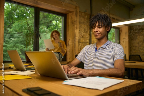Obraz Adult man working on a laptop at a wooden desk