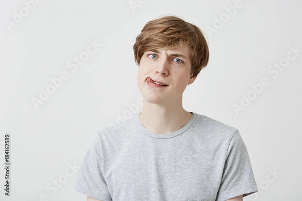 Fototapeta Surprised fair-haired guy dressed casually looks confused, shocked, and puzzled, thinks about something strange, thinks, makes hard decision. Human emotions, feelings and face expression.