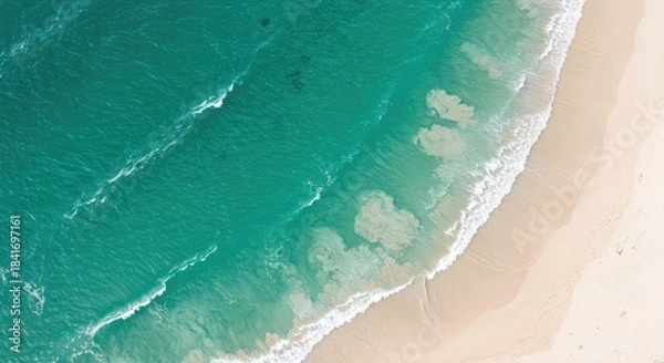 Obraz Aerial view of turquoise ocean waves gently lapping against a pristine sandy beach shore with white foam