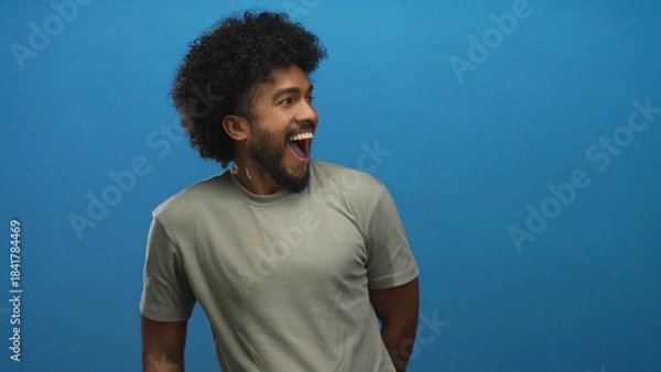 Fototapeta Man with curly hair smiling and pointing against a vibrant blue background exudes confidence and joy