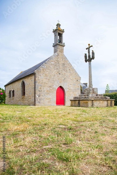 Fototapeta Chapelle Pol, a small granite church in Brignogan-Plages, and the nearby calvary cross and sentry box carved in the rock. Finistere, Brittany, France. Vertical shot.