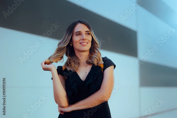 Obraz Happy Confident Woman Wearing a Black Dress Stranding Outdoors. Trendy lady rocking her curly hair outdoors in the city