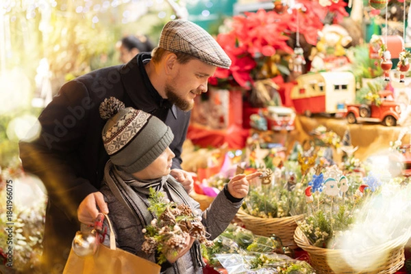 Obraz At Christmas market, dad and son look at bouquets and ikebanas made up of twigs of spruce, pine, eucalyptus. Family walks around bazaar, examines goods, and stares at festive assortment of fair. .