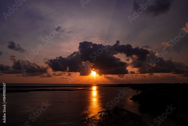 Fototapeta Stunning Sunset Over Calm Ocean With Silhouetted Shoreline, Dramatic Clouds, And Dusk Light