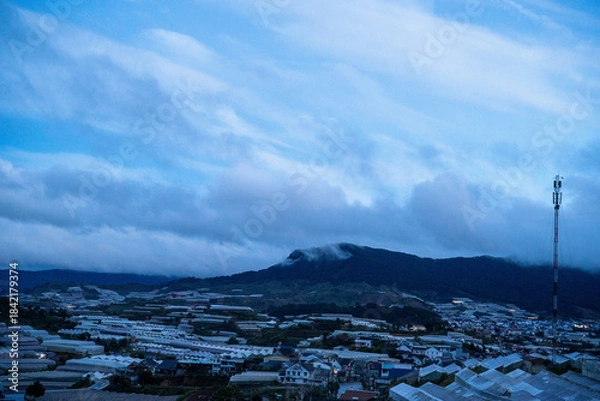 Obraz Scenic view of rolling hills and greenhouses at dusk with soft clouds overhead.