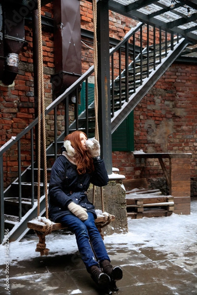Obraz red-haired girl is drinking coffee on  wooden swing in winter street