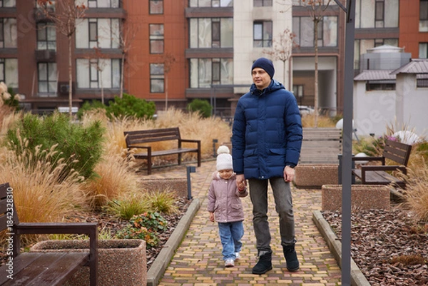 Fototapeta Father and young daughter walking together holding hands in a modern urban park
