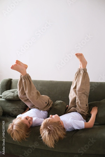 Fototapeta Two boys having fun, lying upside down on the couch, laughing