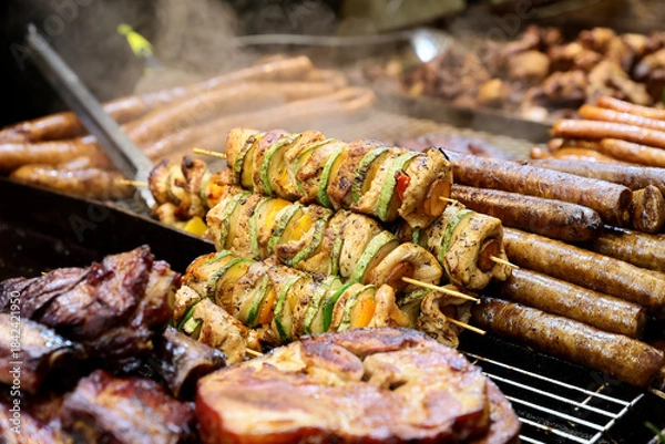 Obraz Grilled chicken kabobs prepared on grill at a Christmas market where various traditional dishes are served.

