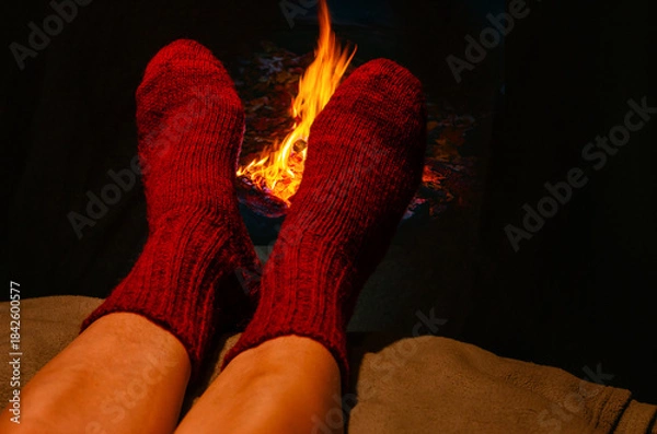 Fototapeta Winter scene with legs in red woolen socks resting near glowing fireplace. Feelings of relaxation.