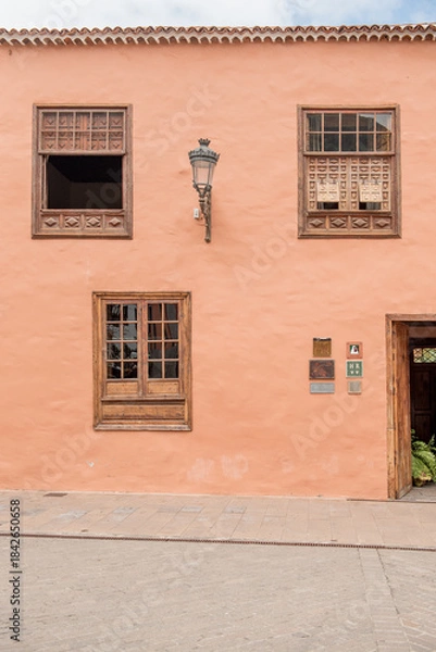 Fototapeta Garachico, Tenerife, Spain - Charming coral-colored building with wooden window frames and traditional architecture, showcasing the beauty of local design