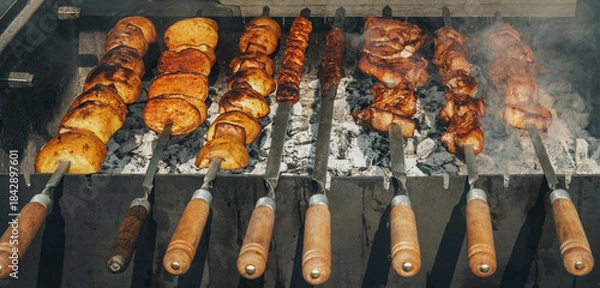 Fototapeta A grill with skewers of meat and potatoes on it