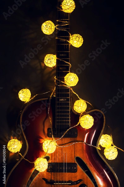 Fototapeta Old electric guitar with a lighted garland on a dark background. Greeting, Christmas, New Year greeting card. Copy space.