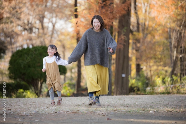 Fototapeta 秋の公園で一緒に娘と手を繋ぐ歩くか走る、ちょっと高齢のママさん