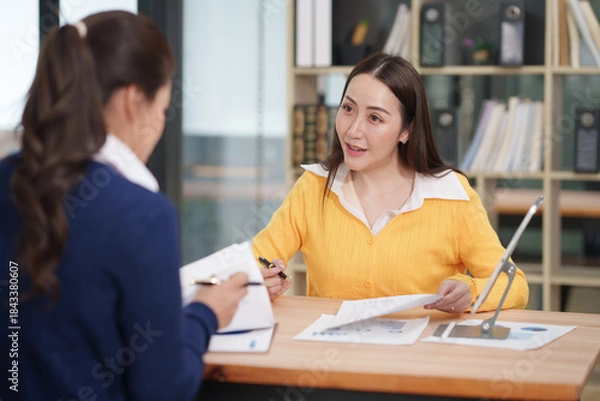 Obraz Asian businesswoman sitting at work using laptop talking and consulting in office
