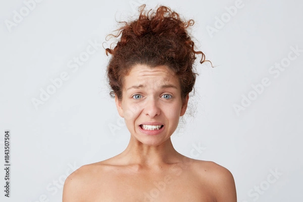 Obraz Close up shot of upset worried young woman with curly hair and healthy skin after applying mask or cream feels confused and embarrassed isolated over white background