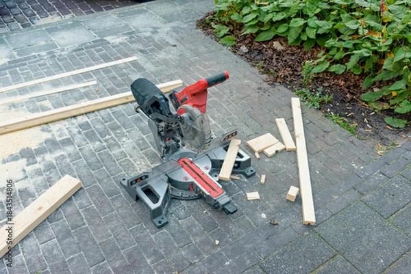 Obraz battery powered miter saw lies outside on the street with wood debris around it