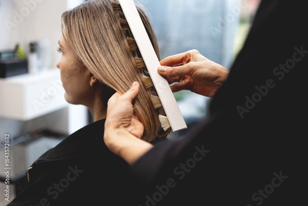 Obraz Hairdresser checking hair color of woman with professional shade chart in modern beauty salon, assessing tones and highlights with precision during color consultation