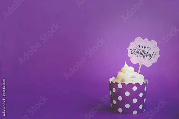 Fototapeta Babeczka waniliowa z małymi ozdobnymi serduszkami i napisem z okazji urodzin, w fioletowym papierowym kubku do pieczenia, na fioletowym tle