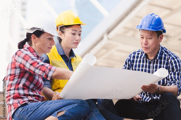Fototapeta Engineers man and woman working on plan building construction in city