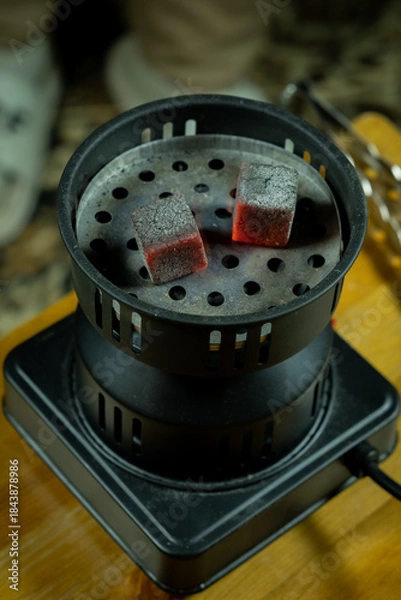 Obraz Hot coals placed in a hookah bowl on a wooden table during a social gathering in the evening