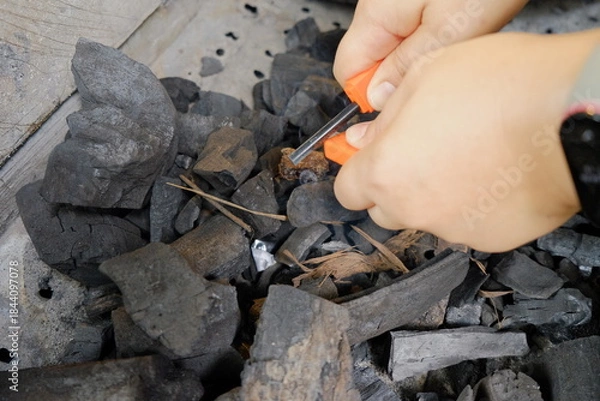 Obraz Hands using a fire starter tool to prepare charcoal for grilling